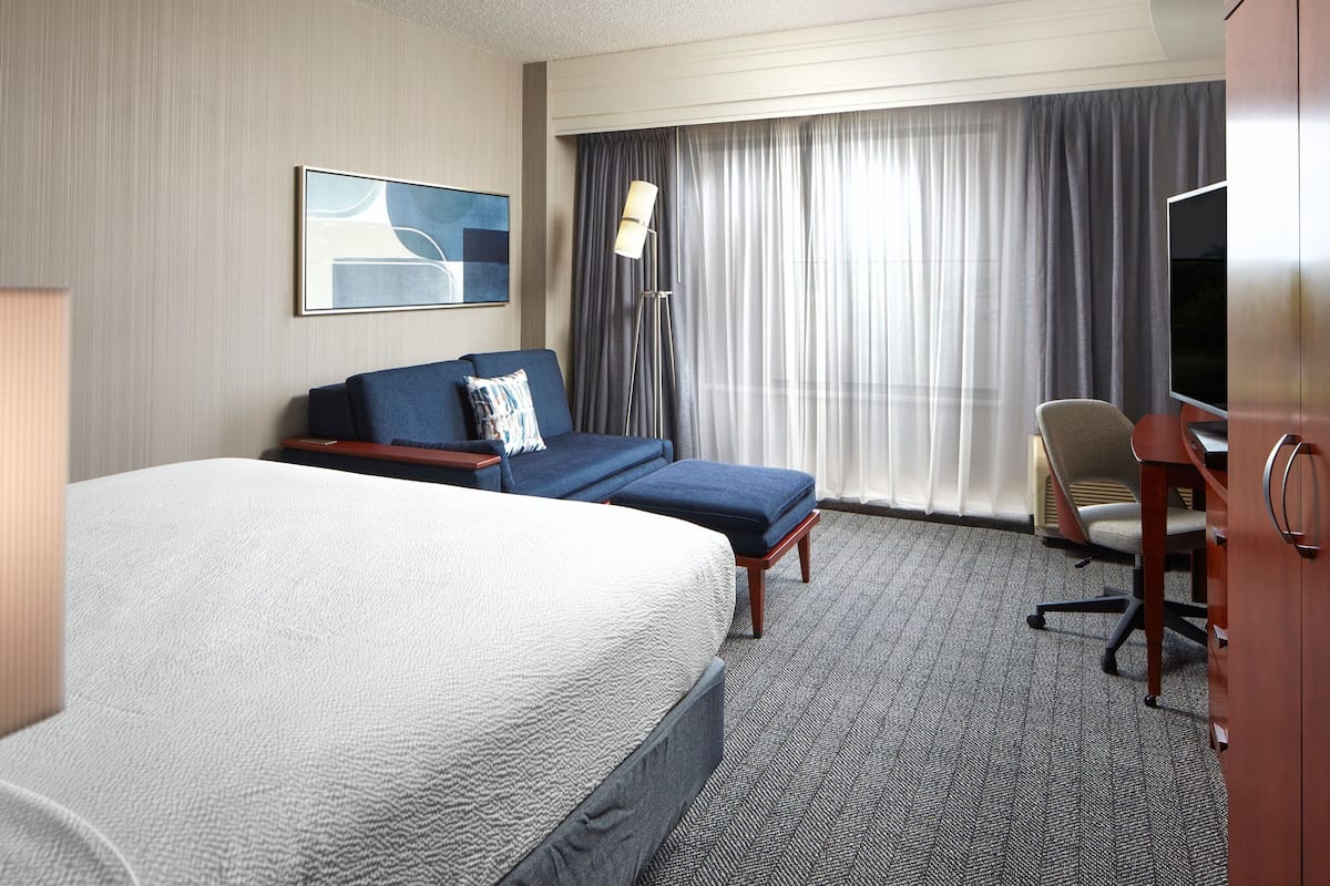 A hotel room with a large bed, a sofa, a desk, a chair, and a television.
