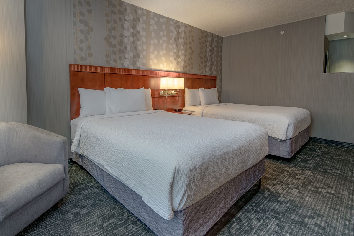 Une chambre d’hôtel avec deux lits, une chaise et une table de chevet avec une lampe.