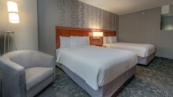 A hotel room with two beds, a chair, and a nightstand with a lamp.