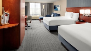 A hotel room with two beds, a desk, a chair, a desk lamp, and a large window with curtains. - Courtyard by Marriott Winchester (Winchester)