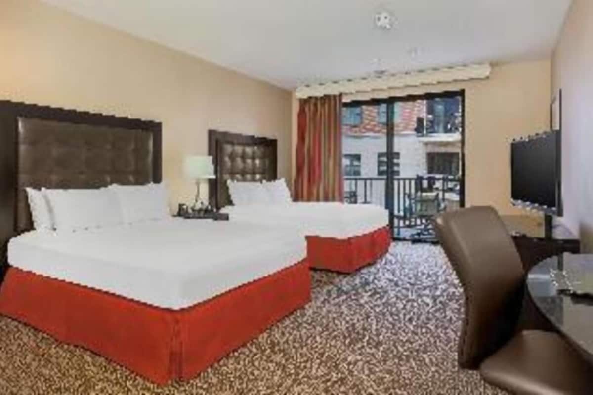 A hotel room with two beds, a TV, and a balcony with a view.