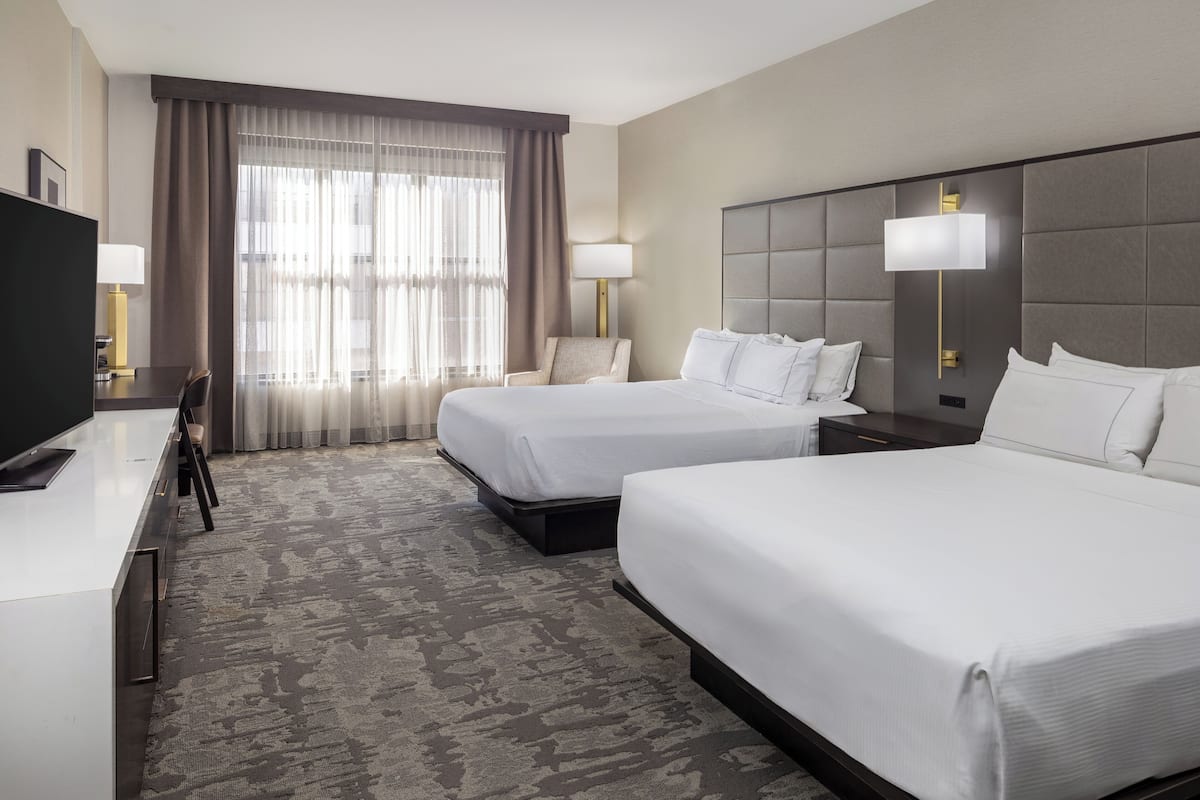 A hotel room with two beds, a desk, a chair, and a TV.