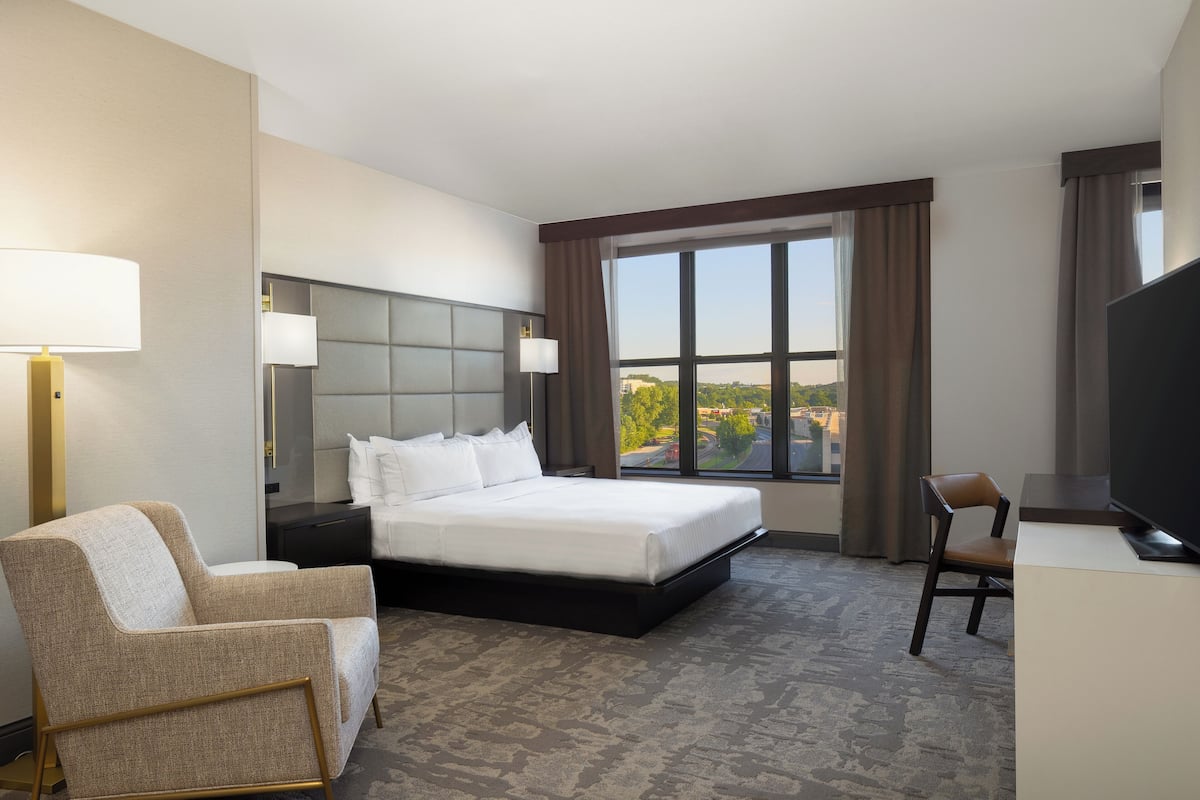 A hotel room with a large bed, a chair, a desk, and a TV.
