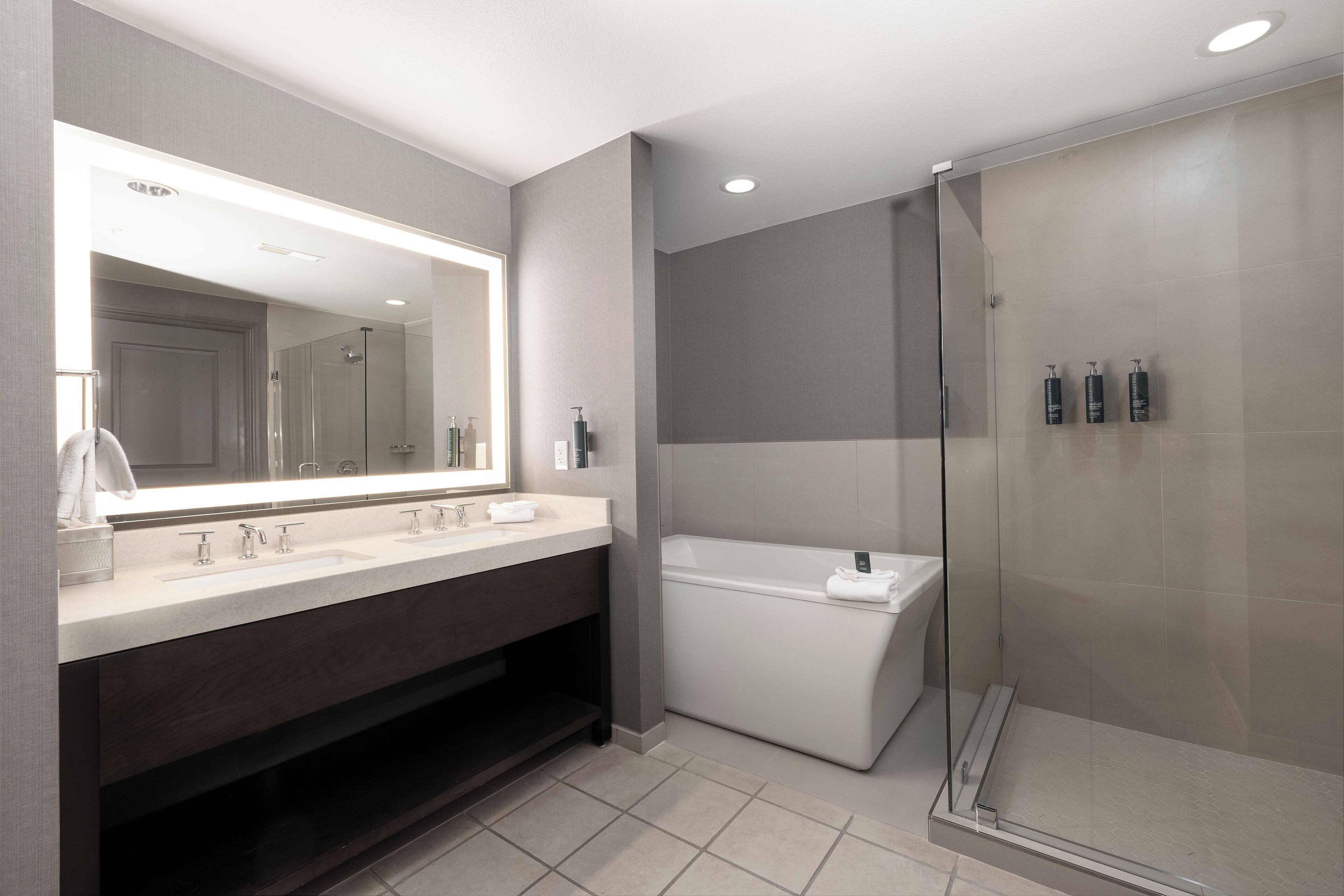 A modern bathroom with a large mirror, dual sinks, a glass-enclosed shower, and a vanity with a dark wood cabinet.