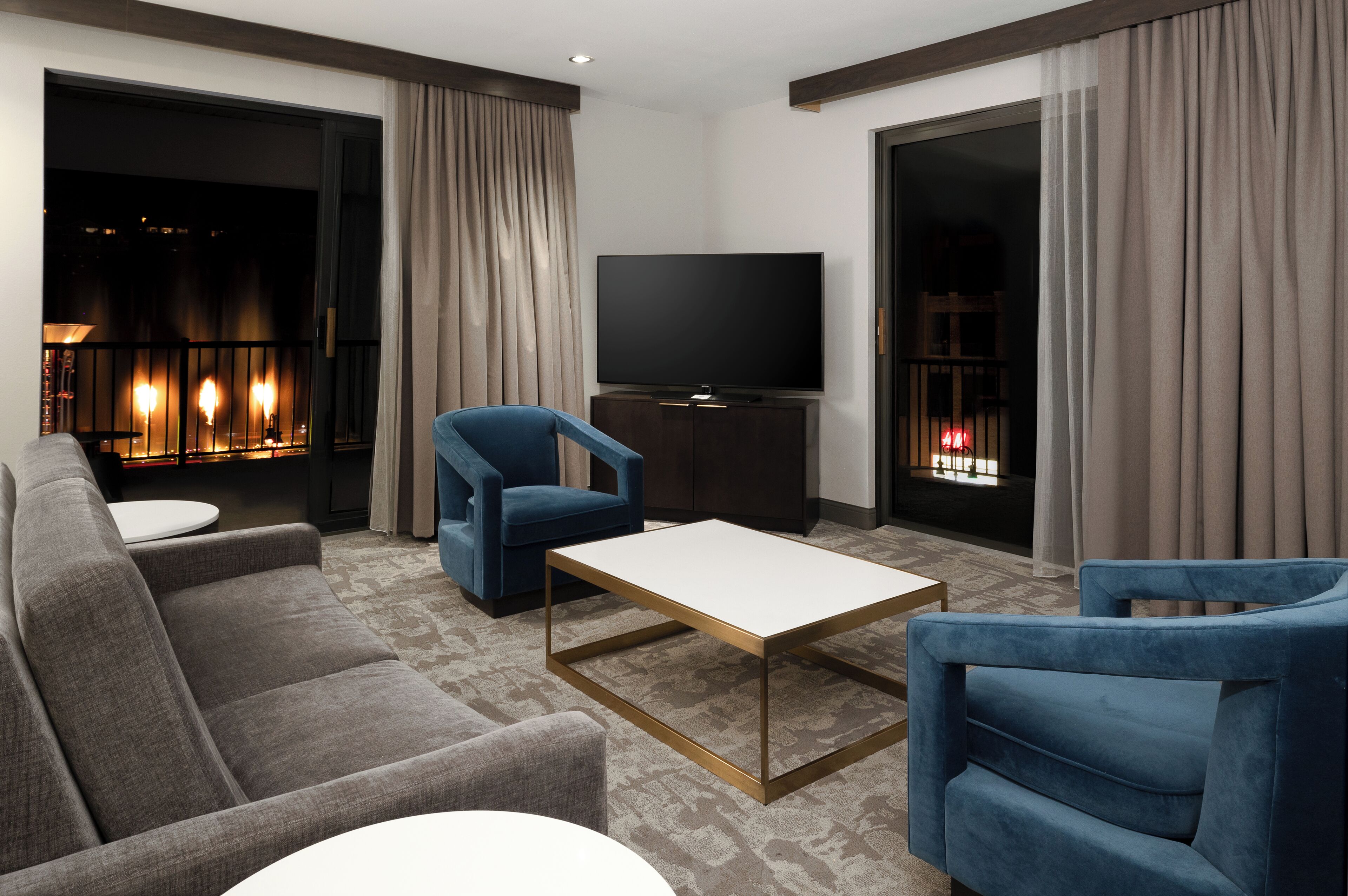 A modern living room with a sofa, two blue armchairs, a coffee table, and a TV.