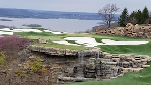 A golf course with a waterfall feature, a pond, and a view of a lake. - Hilton Promenade at Branson Landing (Branson)