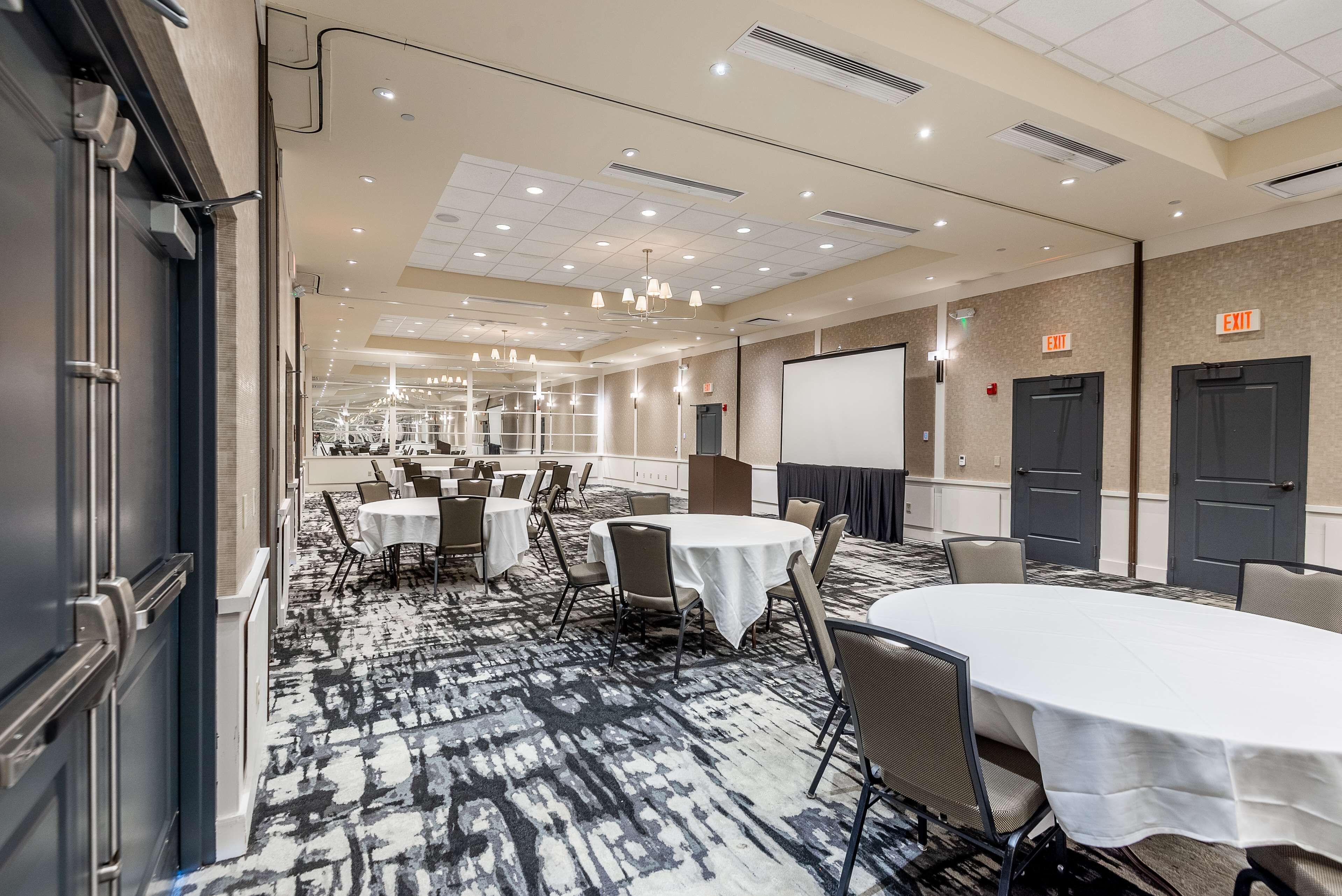 A conference room with multiple tables and chairs, a whiteboard, and an exit door.