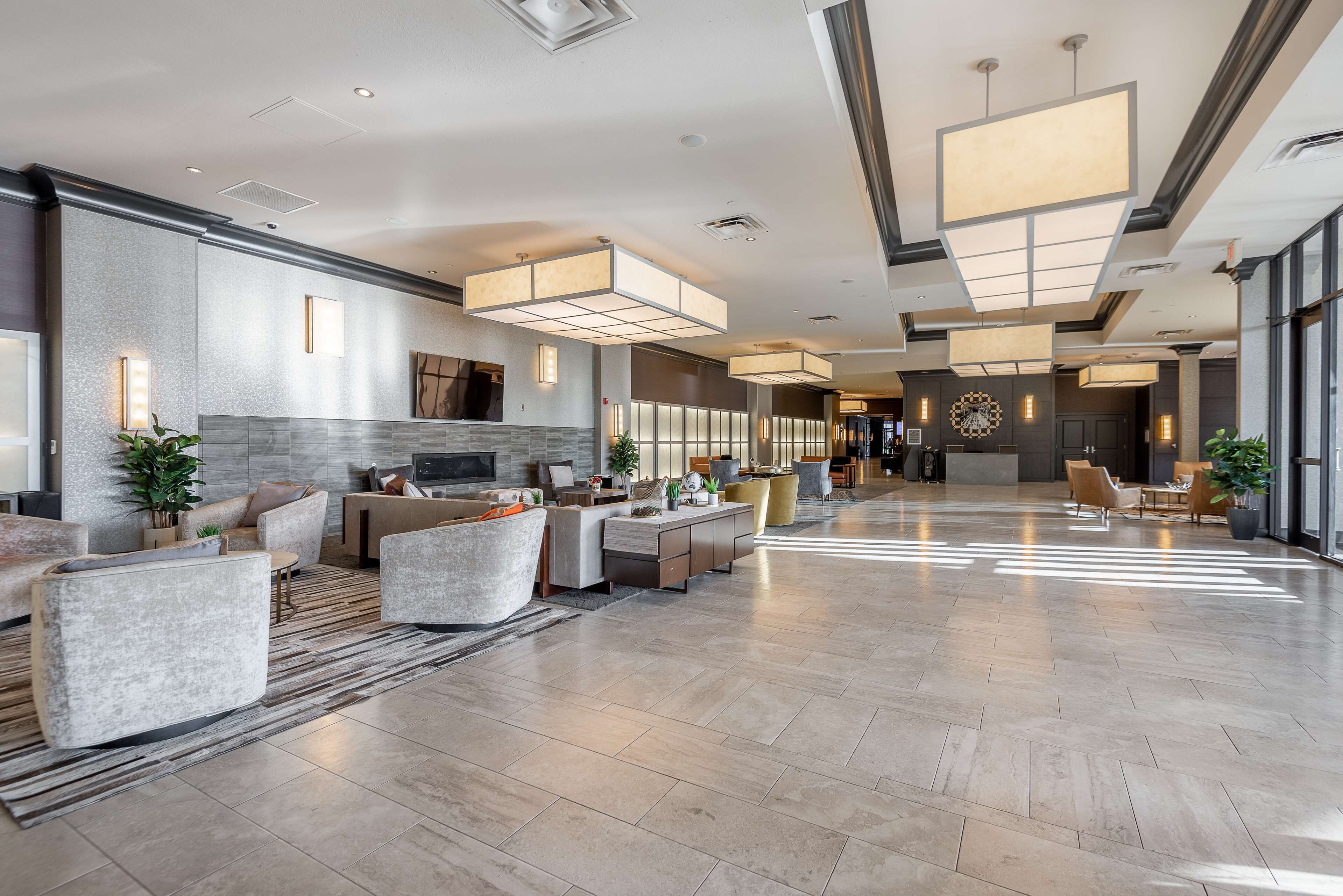 A spacious lobby with a modern design, featuring a mix of seating areas, a fireplace, and large windows allowing natural light.
