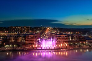 A nighttime cityscape with a fountain in the foreground and buildings in the background. - Hilton Promenade at Branson Landing (Branson)