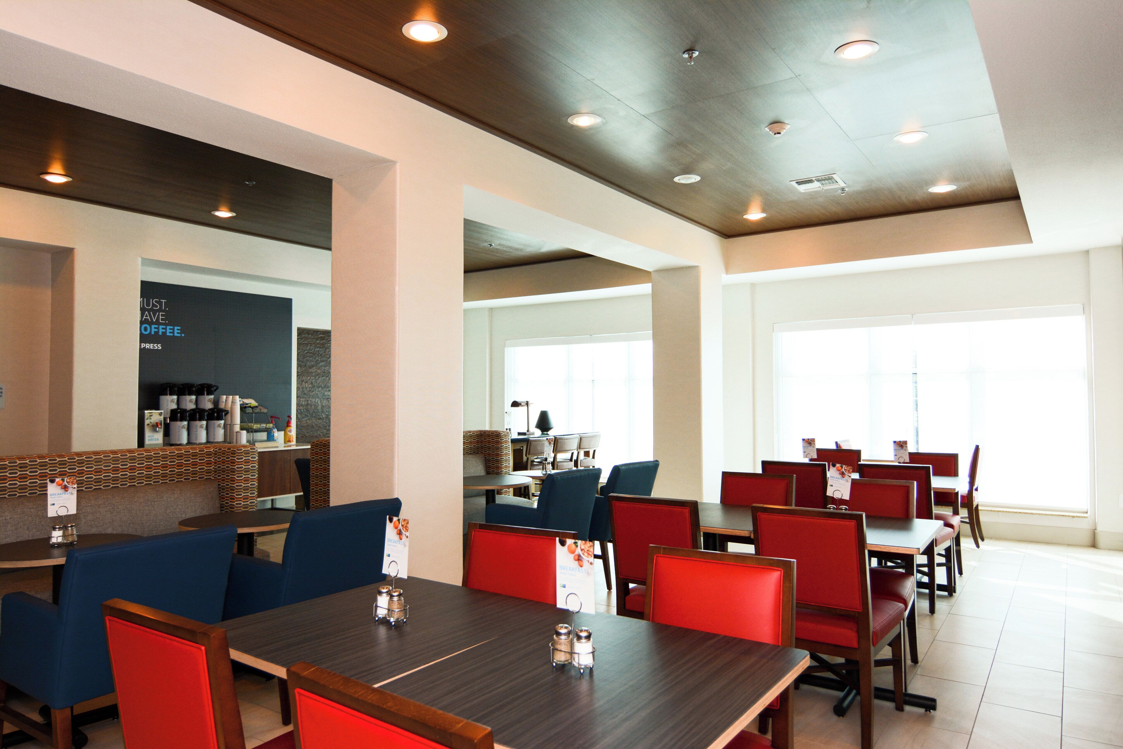 A modern restaurant with high ceilings, recessed lighting, and a mix of red and blue seating.