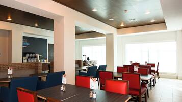 A modern restaurant with high ceilings, recessed lighting, and a mix of red and blue seating.