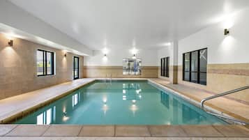 An indoor swimming pool with clear water, surrounded by walls with windows and a tiled floor.
