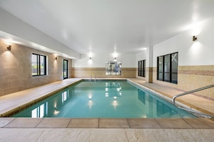 Una piscina interior con agua cristalina, rodeada por paredes con ventanas y un suelo de baldosas.