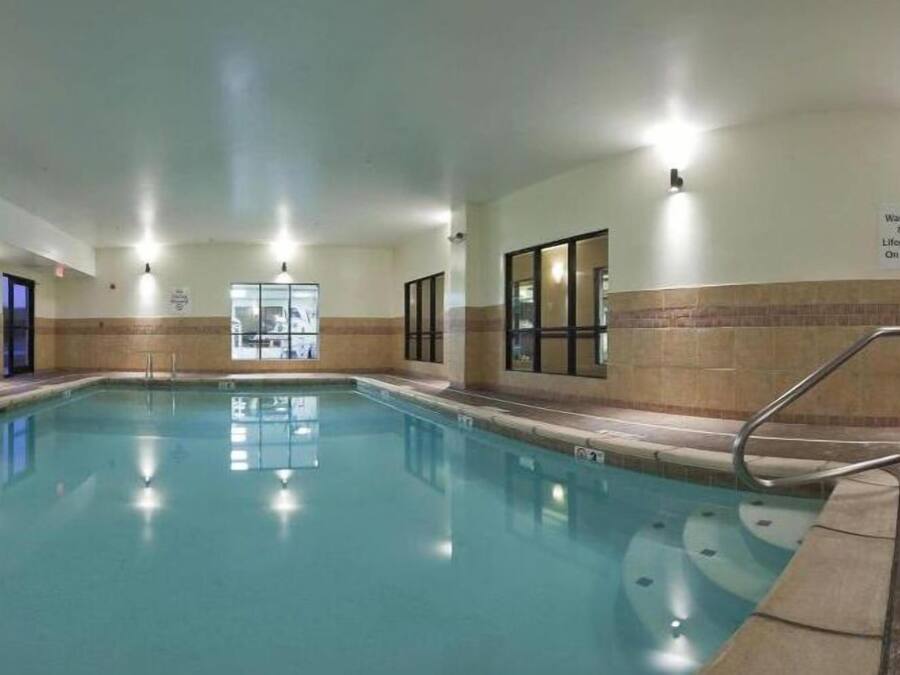 An indoor swimming pool with clear water, surrounded by walls with windows and a lifeguard sign.