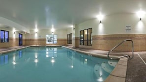 Une piscine intérieure à l’eau claire, entourée de murs percés de fenêtres et agrémentée d’un panneau indiquant la présence d’un sauveteur.