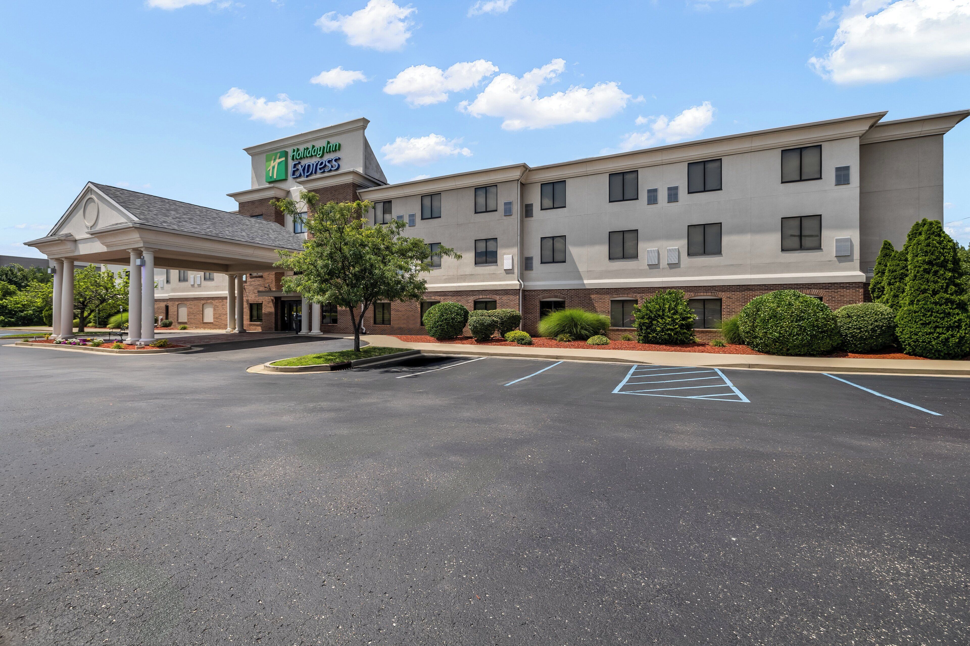 Um hotel Holiday Inn Express com entrada coberta, parque de estacionamento e áreas ajardinadas.