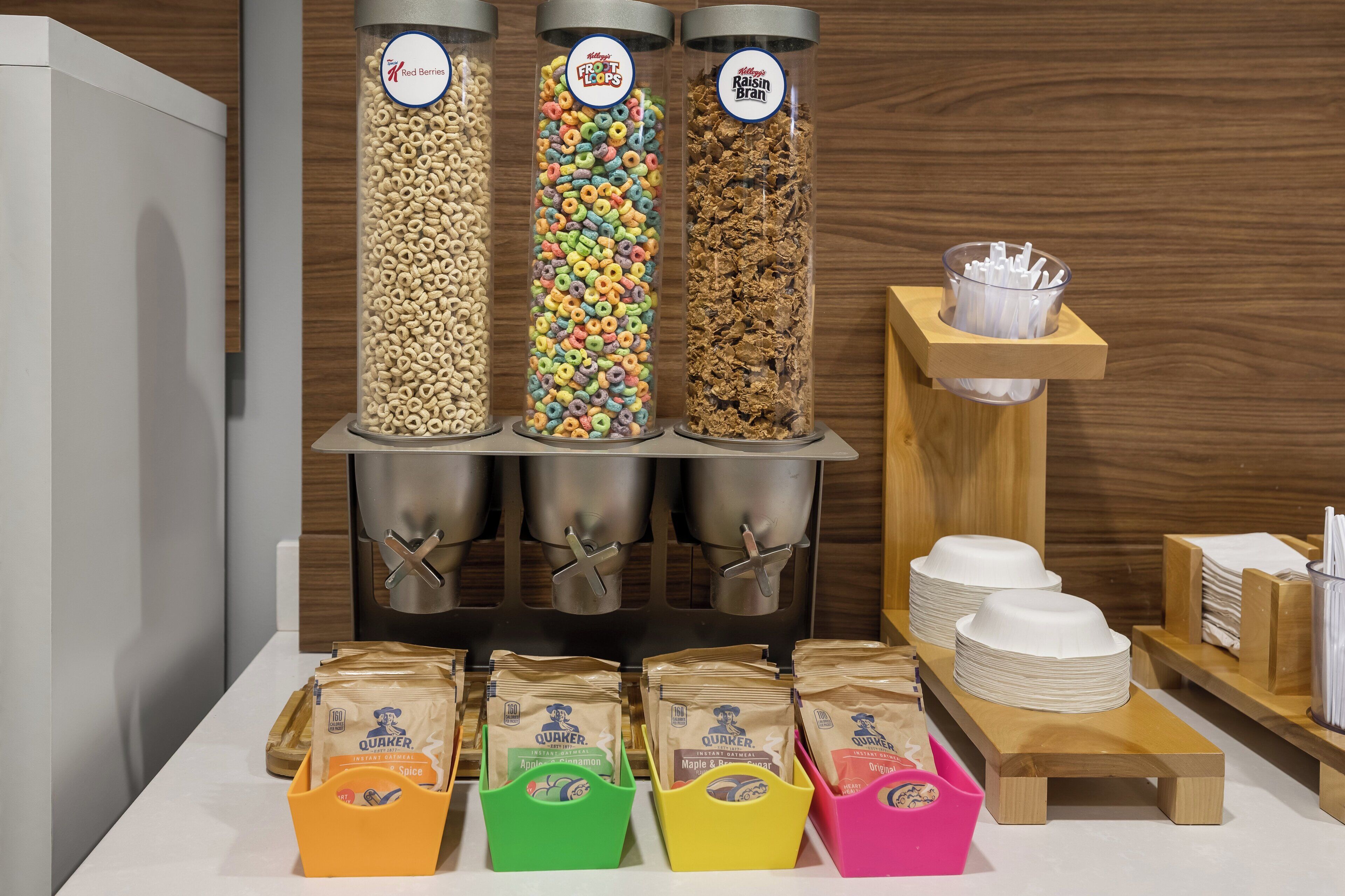 Una exhibición de alimentos con tres recipientes de cereal y paquetes de avena instantánea.