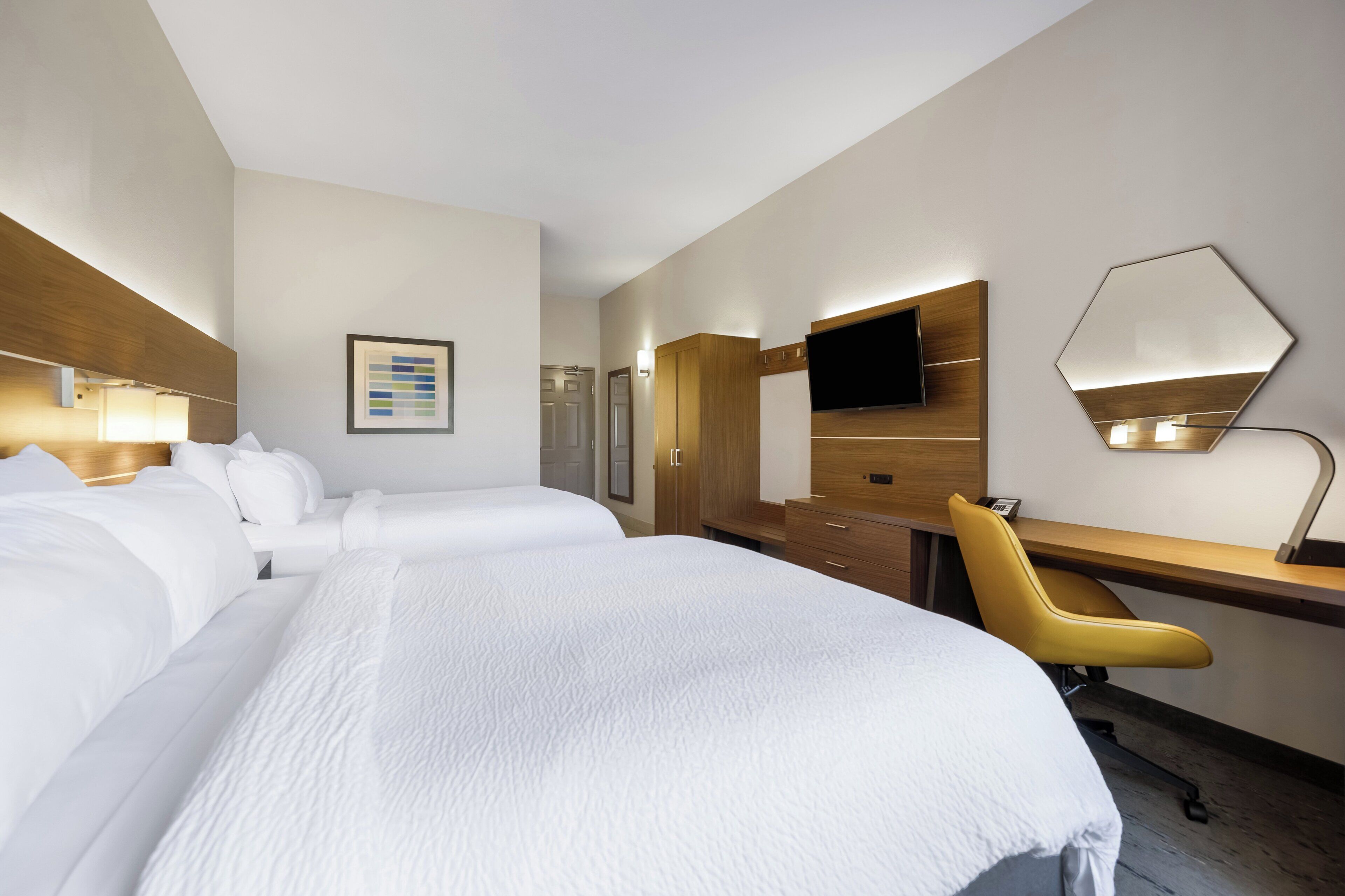 A hotel room with two beds, a desk, a chair, a flat-screen TV, and a mirror.