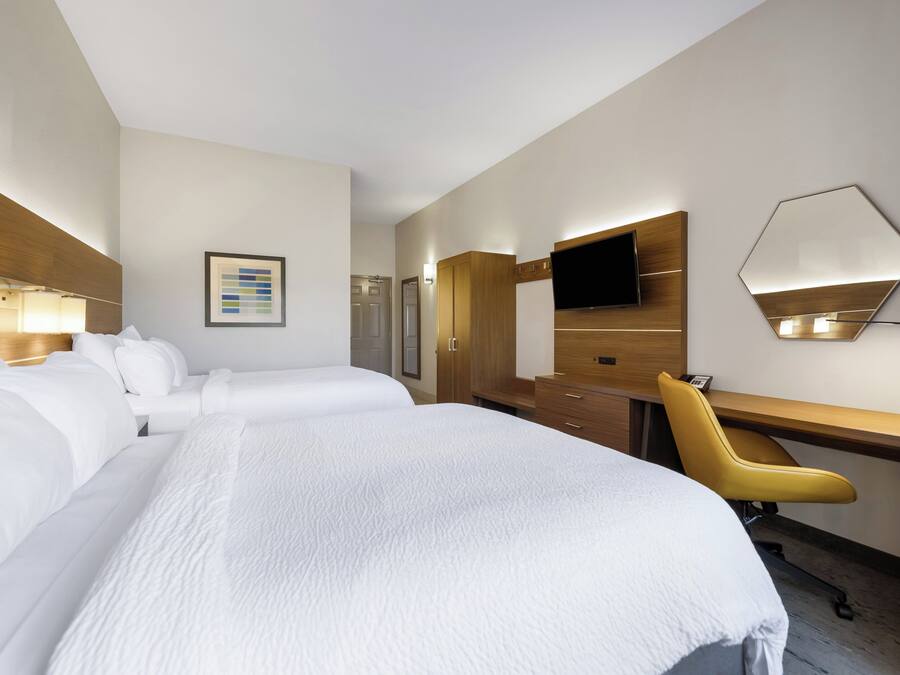 A hotel room with two beds, a desk, a chair, a flat-screen TV, and a mirror.