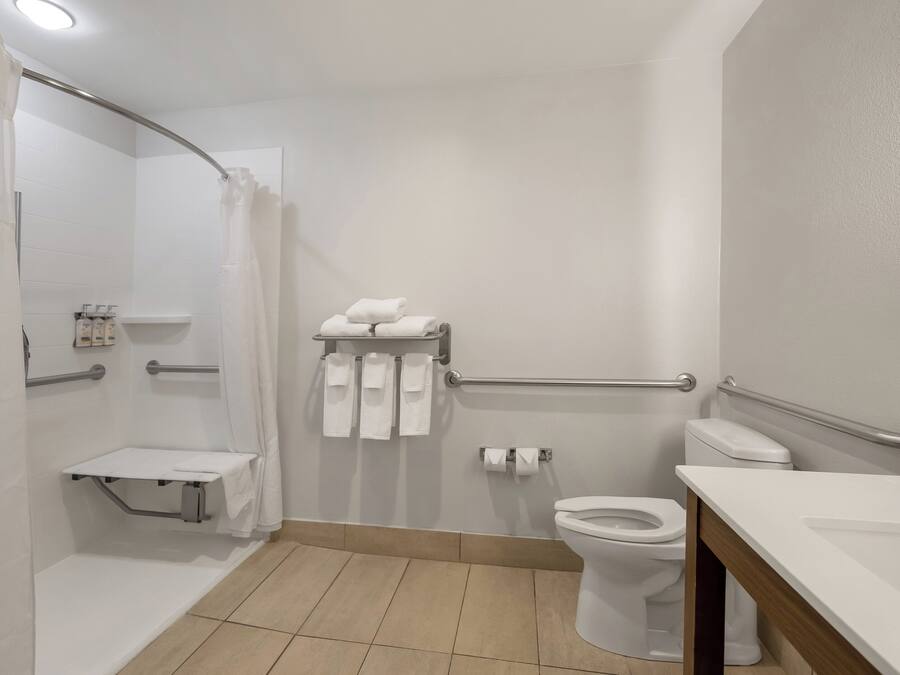 Un baño con inodoro, lavamanos, zona de ducha y barra de apoyo.