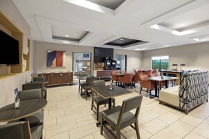 Un comedor moderno con mesas y sillas, una estación de café y un televisor de pantalla plana montado en la pared.