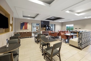 A modern dining area with tables and chairs, a coffee station, and a flat-screen TV mounted on the wall.