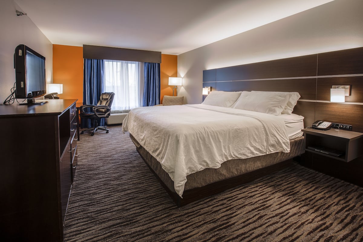 A hotel room with a large bed, a desk with a computer, a chair, a TV, and a phone on the nightstand.