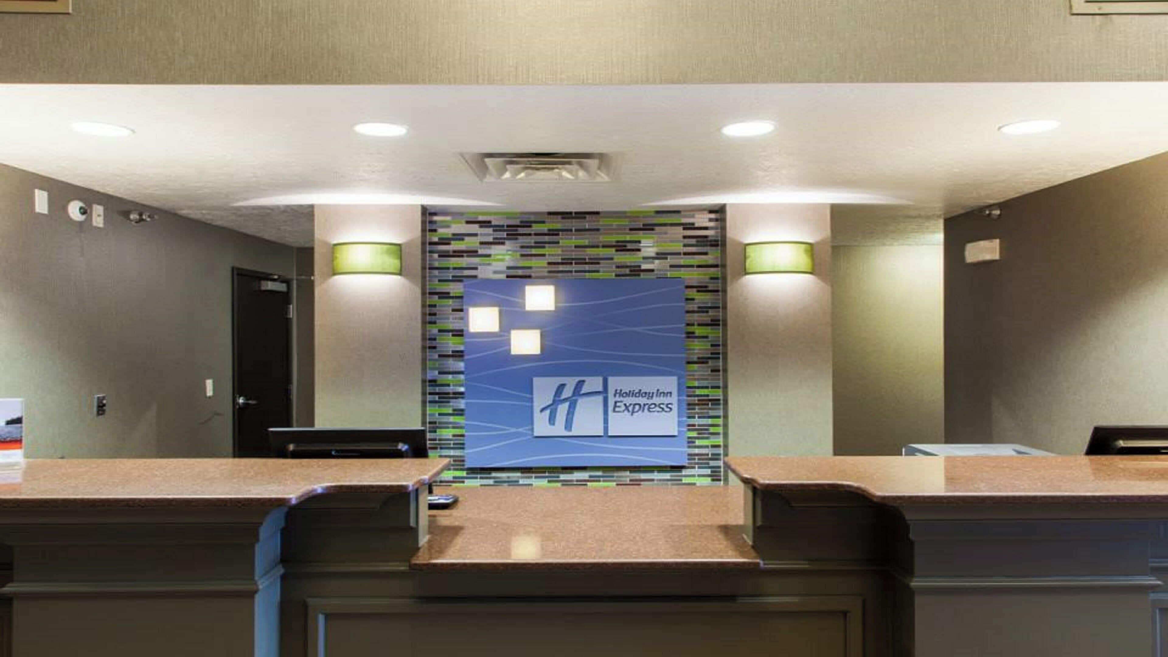 Zona de recepción con letrero de Holiday Inn Express, un mostrador de recepción y dos lámparas fijadas a la pared.