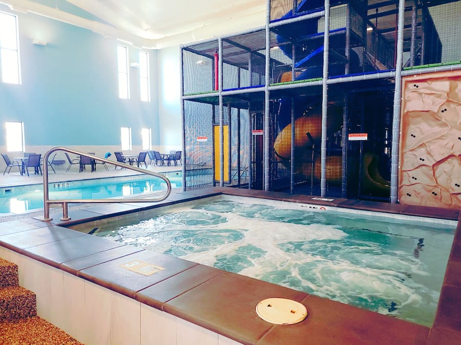 An indoor swimming pool with a hot tub, surrounded by a play area with safety railings.