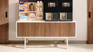 A reception desk with a wooden finish, a white countertop, and a shelf with various items including a coffee machine. - Holiday Inn Express & Suites Brandon by IHG (Brandon)