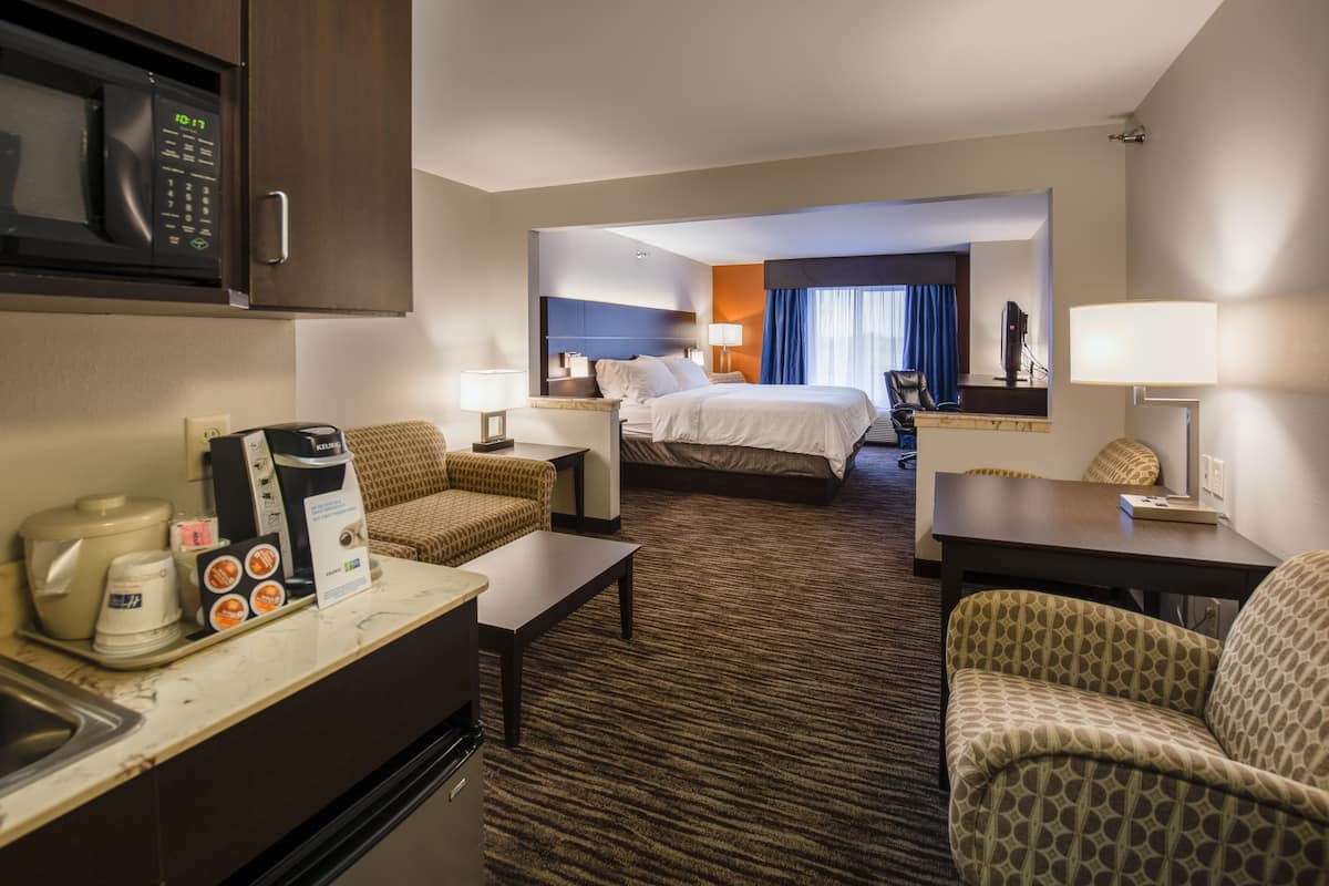A hotel room with a bed, a desk, a chair, a microwave, a coffee maker, and a television.
