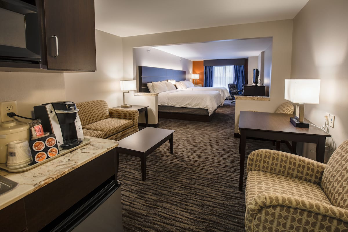 A hotel room with a kitchenette, two beds, a sofa, a coffee maker, and a lamp.