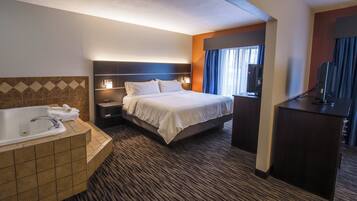 A hotel room with a large bed, a separate bathroom with a bathtub, a desk with a computer, and a window with curtains.