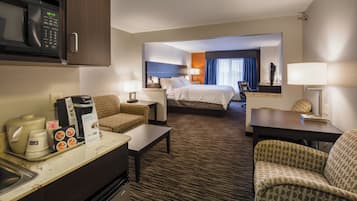 Una habitación de hotel con cama, dos sillas, escritorio, microondas y cafetera.