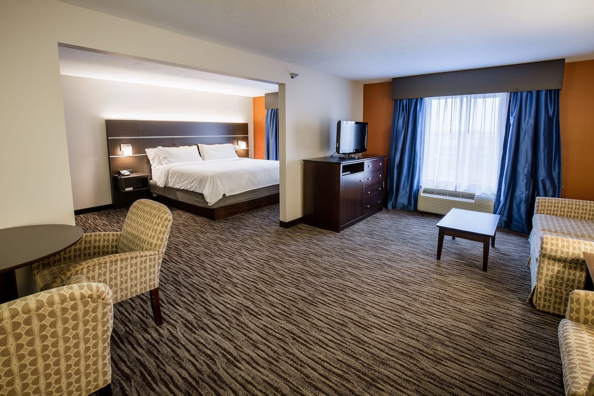 A hotel room with a bed, a television on a cabinet, a desk, and two armchairs.