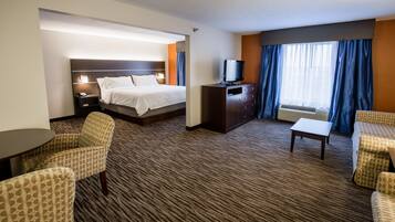 Una habitación de hotel con una cama, un televisor en un mueble, un escritorio y dos sillones.