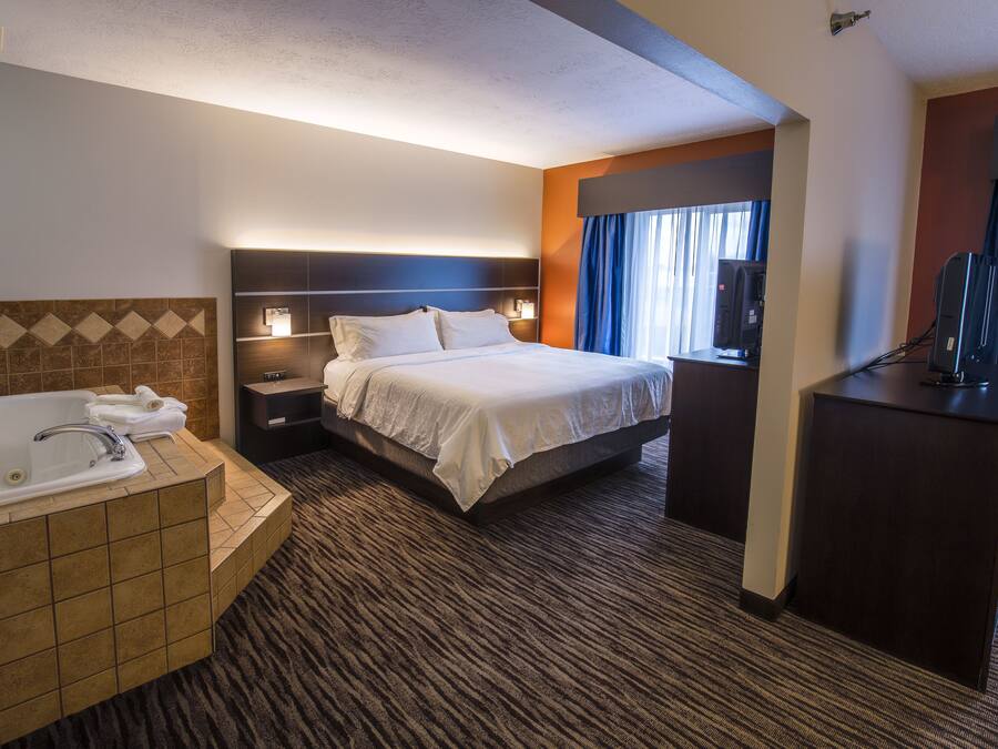 A hotel room with a large bed, a separate bathroom with a bathtub, a desk, and a television.