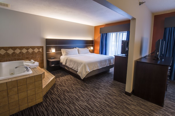 Quarto de hotel com uma cama grande, banheiro separado com banheira, escrivaninha e televisão.