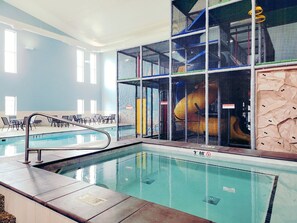 An indoor swimming pool with a diving board, seating area, and a play structure visible through a safety screen. - Holiday Inn Express & Suites Brandon by IHG (Brandon)