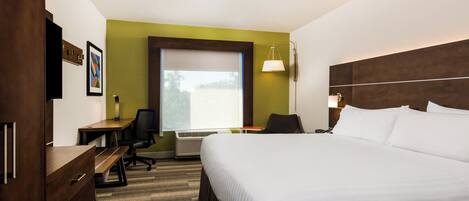 A hotel room with a large bed, a desk, a chair, a desk lamp, and a window.