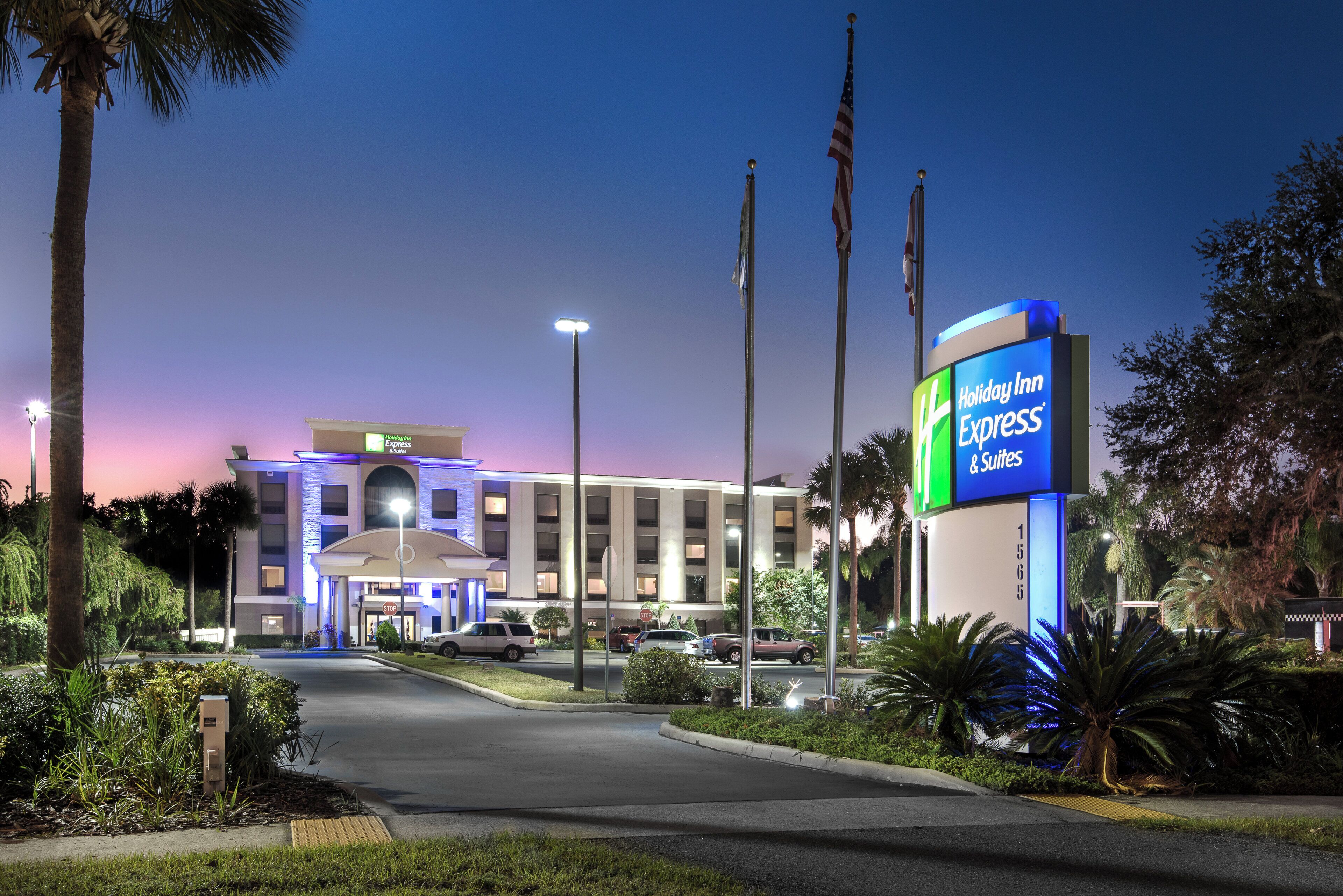 A Holiday Inn Express & Suites hotel with a well-lit entrance, a parking area, and a clear sky.