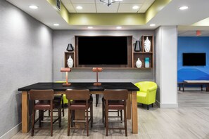 Uma sala de conferências com uma grande televisão de tela plana, cadeiras de madeira, uma mesa preta e uma cadeira amarelo-vivo.