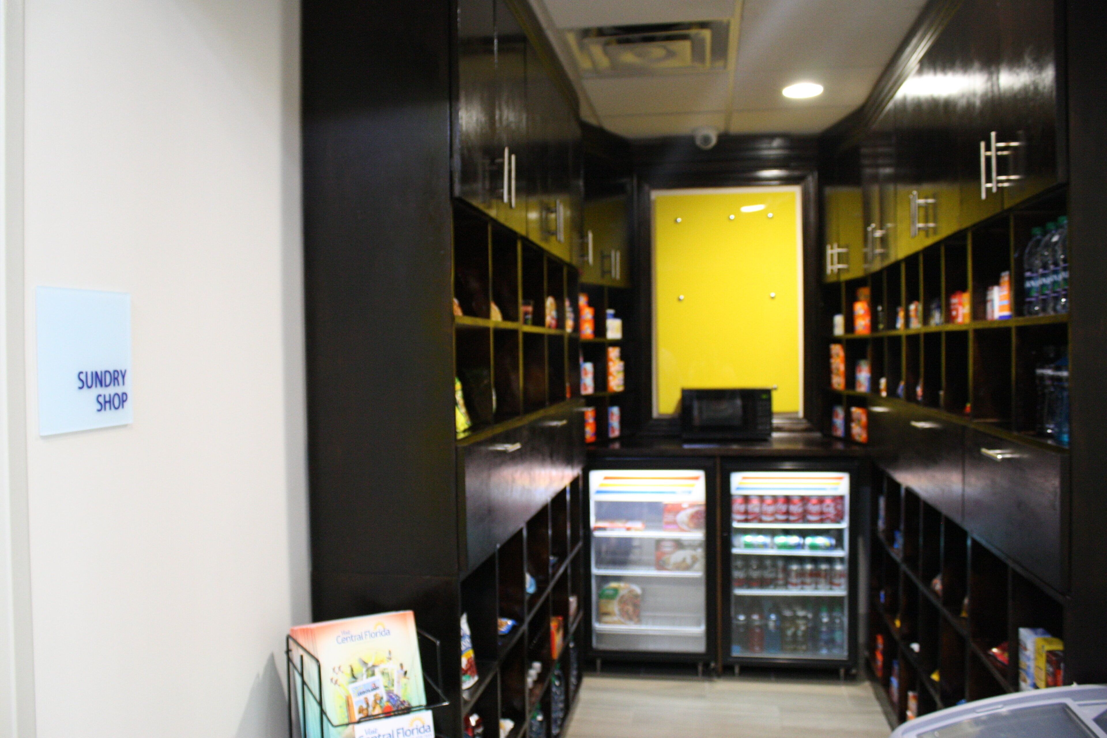 A corridor with shelves on both sides, a refrigerator at the end, and a sign on the left wall.