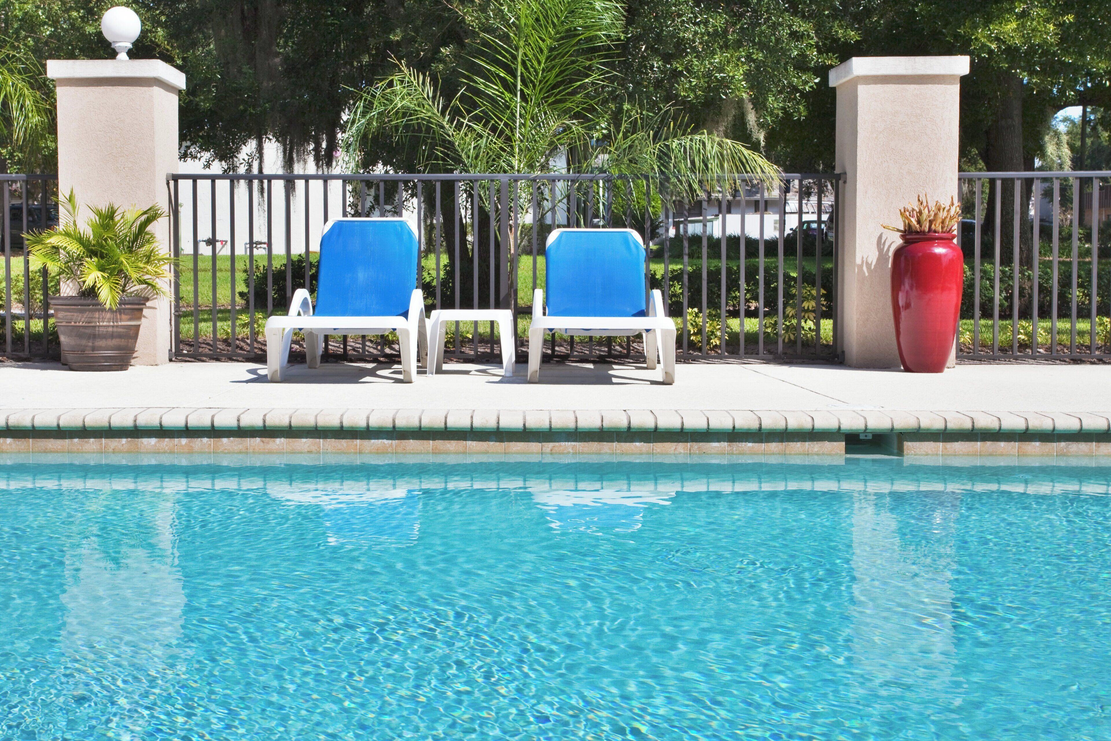 A swimming pool with two lounge chairs and a red vase on the side.