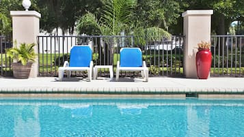 A swimming pool with two lounge chairs and a red vase on the side.