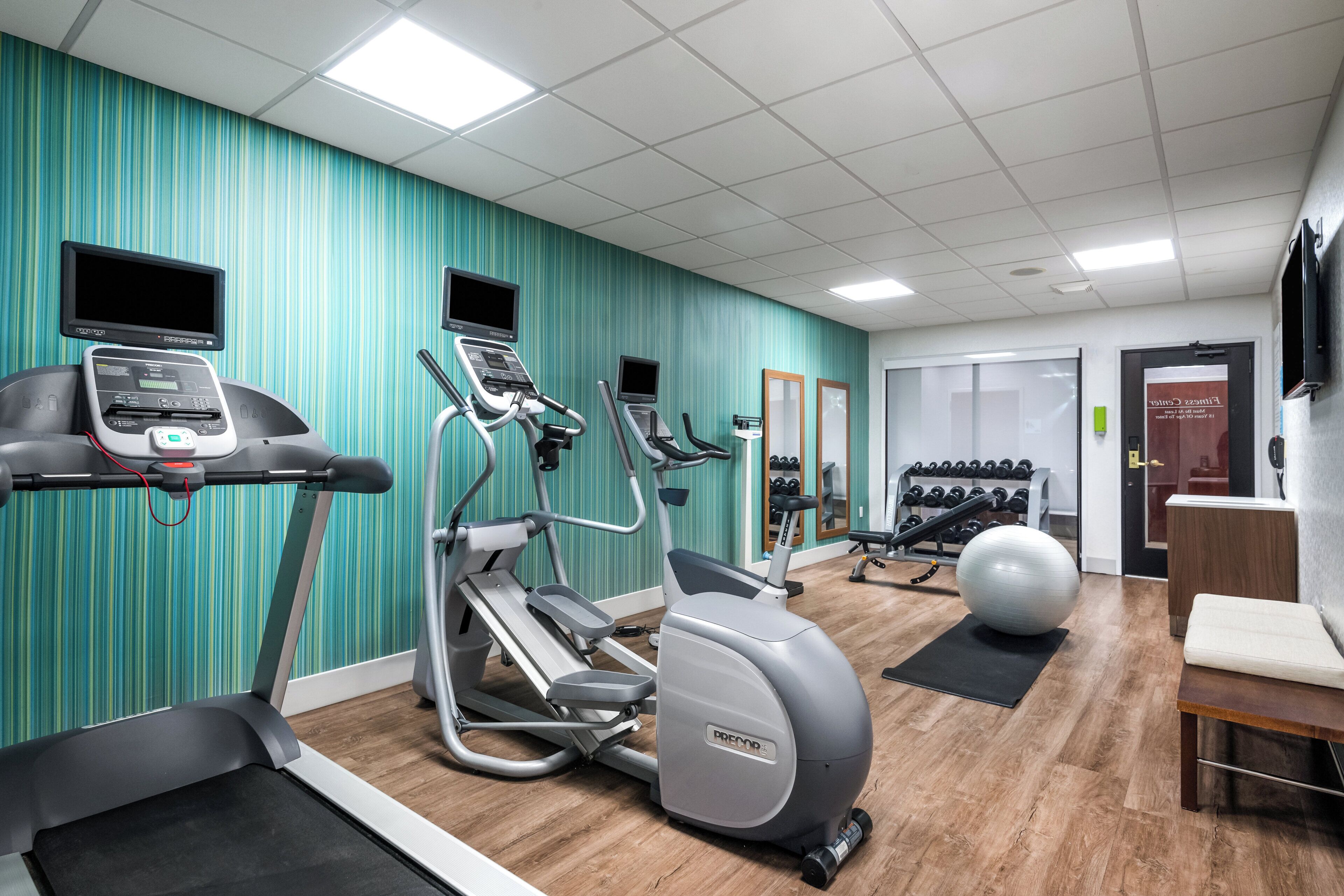 A gym with various exercise equipment, including treadmills, elliptical machines, and a stationary bike.