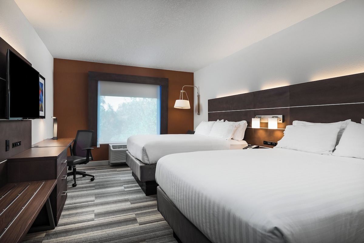 A hotel room with two beds, a desk, a chair, a TV, and a window with a view.