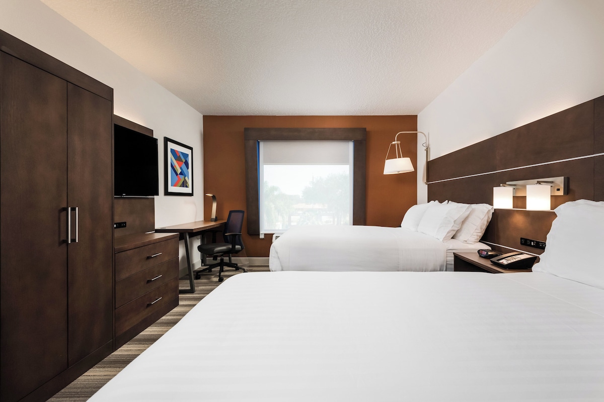 A hotel room with a bed, desk, chair, wardrobe, TV, and a window with a view.