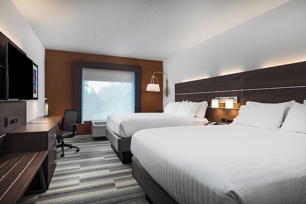 A hotel room with two beds, a desk, a chair, a TV, and a window with a view of trees.