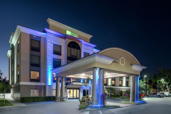 A Holiday Inn Express hotel with a modern facade, a covered entrance, and a landscaped area with plants and a bench.